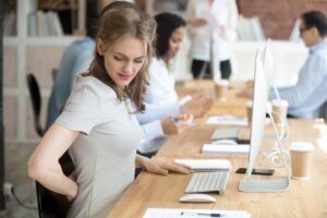 Millennial business woman feels discomfort sitting in chair shared office. Female massaging her back suffering from ache