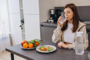 Young woman enjoying a healthy meal with fresh salad and drinking water, promoting a healthy lifestyle in her modern kitchen