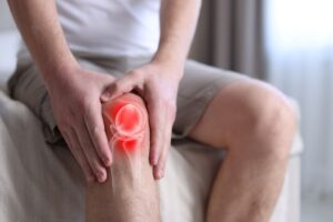 Arthritis. Man suffering from knee pain on bed indoors, closeup. Illustration of joint inflammation on his leg