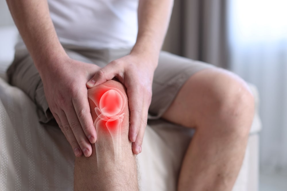 Arthritis. Man suffering from knee pain on bed indoors, closeup. Illustration of joint inflammation on his leg